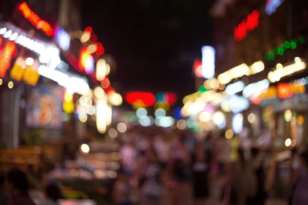 Blurred neon signs and string lights on a busy bar street at night
