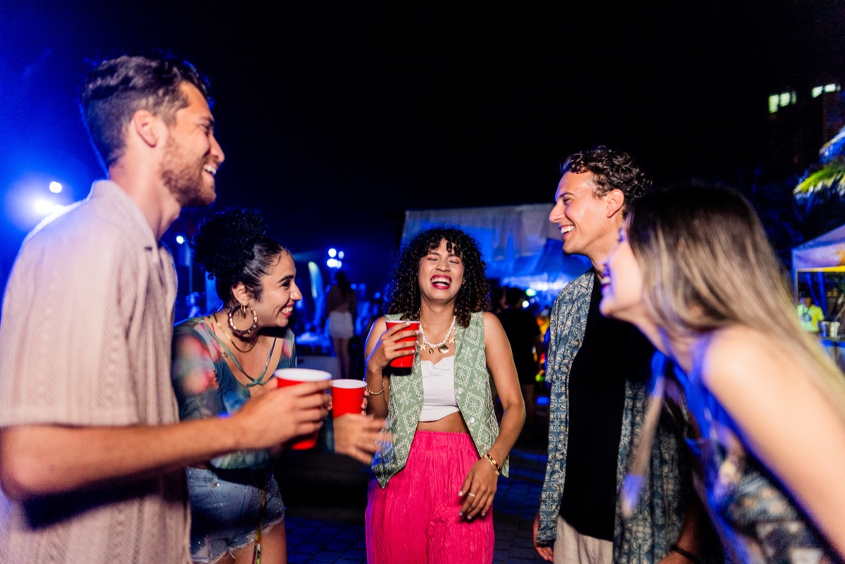 A group of friends laughing with drinks in hand at an outdoor bar at night in San Benito, San Salvador