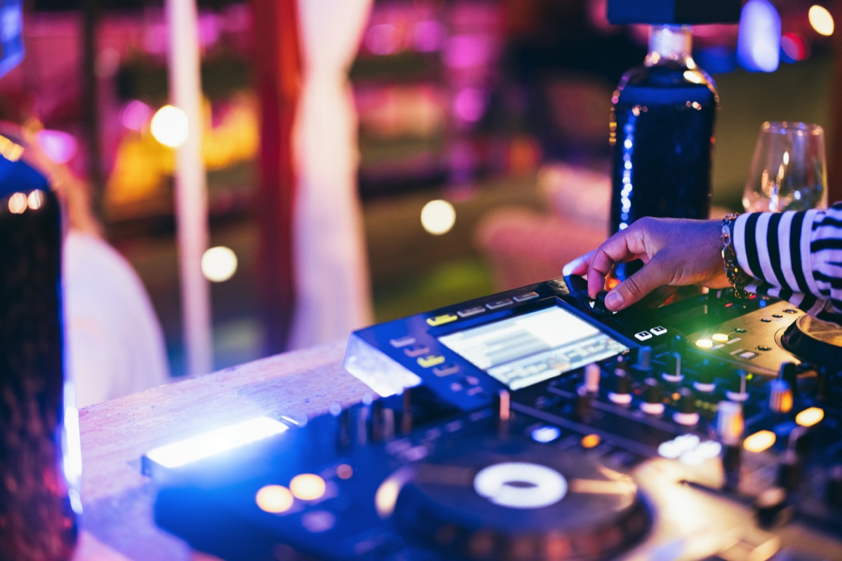 A DJ's hand on the decks under pink and blue lights in a Zona Rosa club, San Salvador